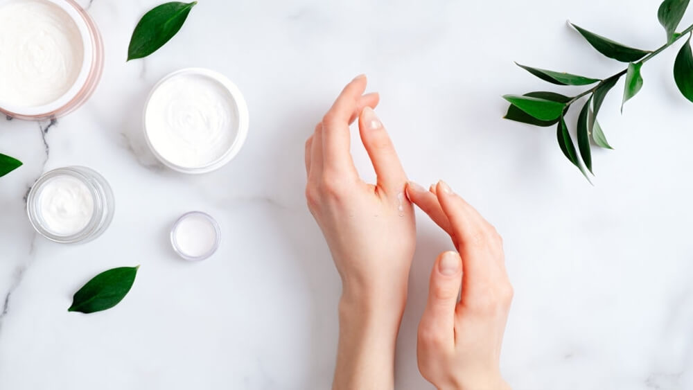 Cosmetic cream on female hands jars with milk swirl cream and green leaves on white table