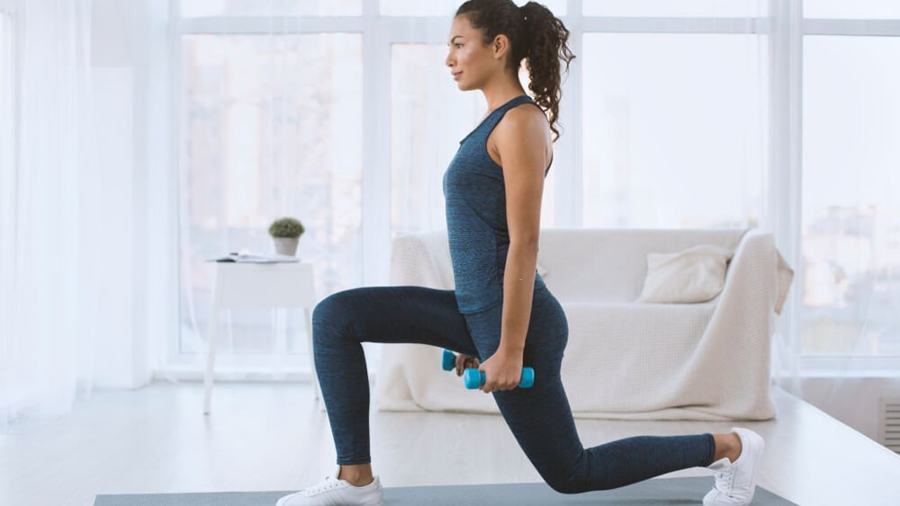 Slim hispanic girl doing lunges with dumbbells at home