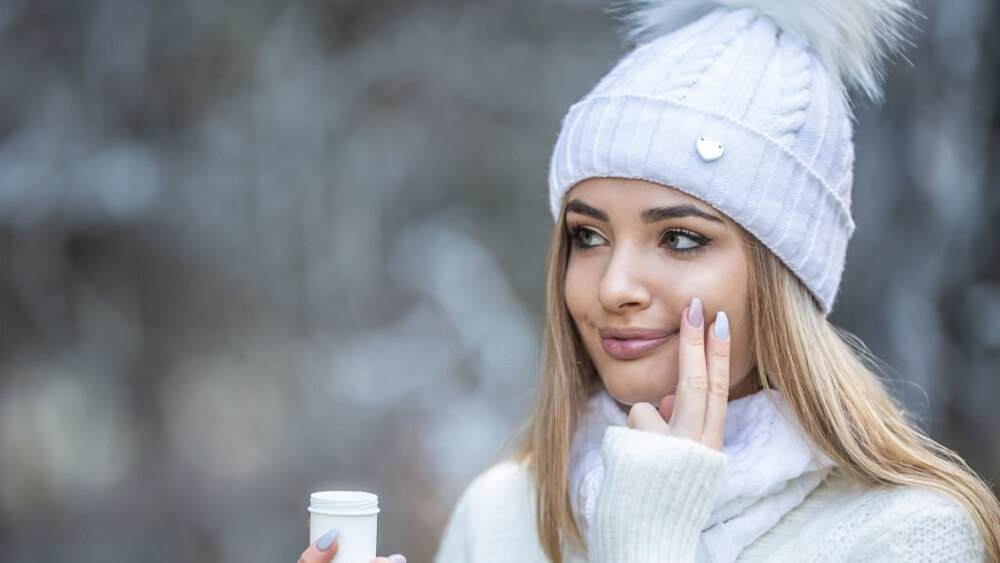 Beautiful girl applied face-cream on her cheek in winter
