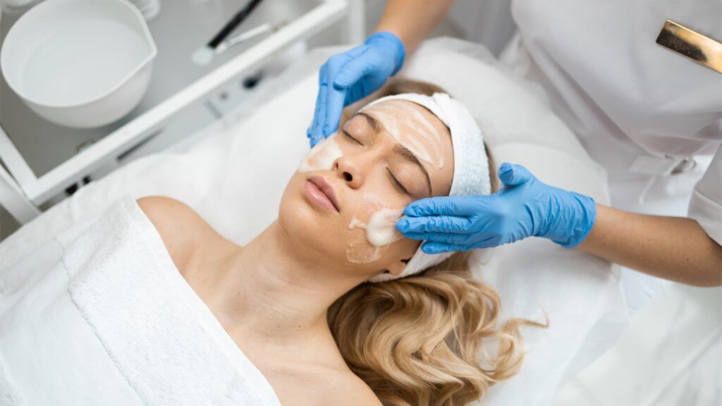 Beautician doctor in blue gloves is doing facial treatment