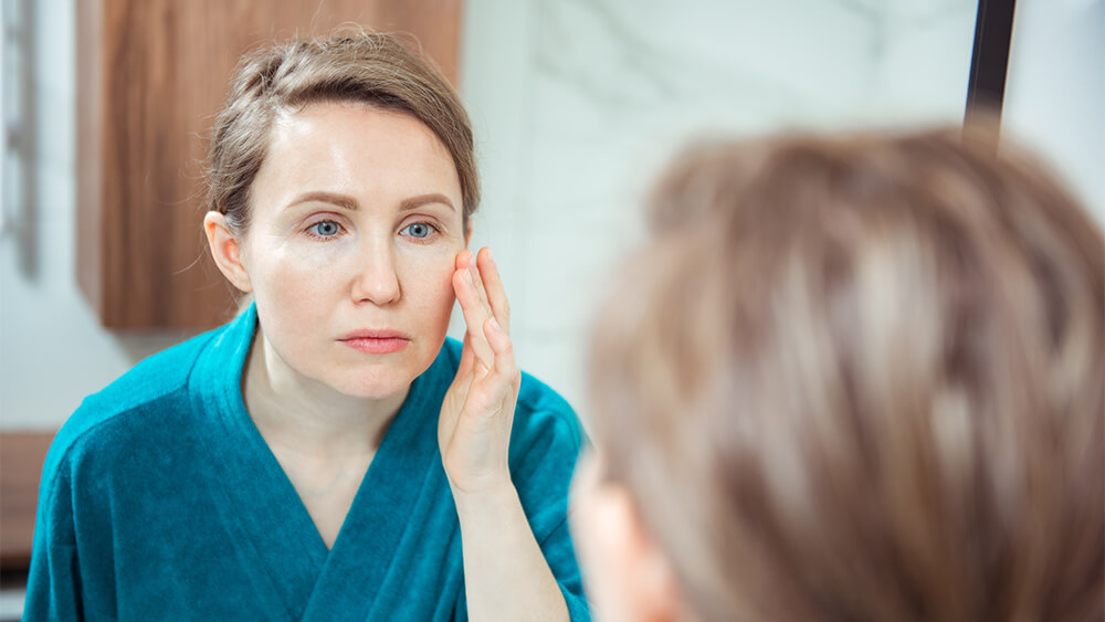 Unhappy woman looking her skin in the mirror