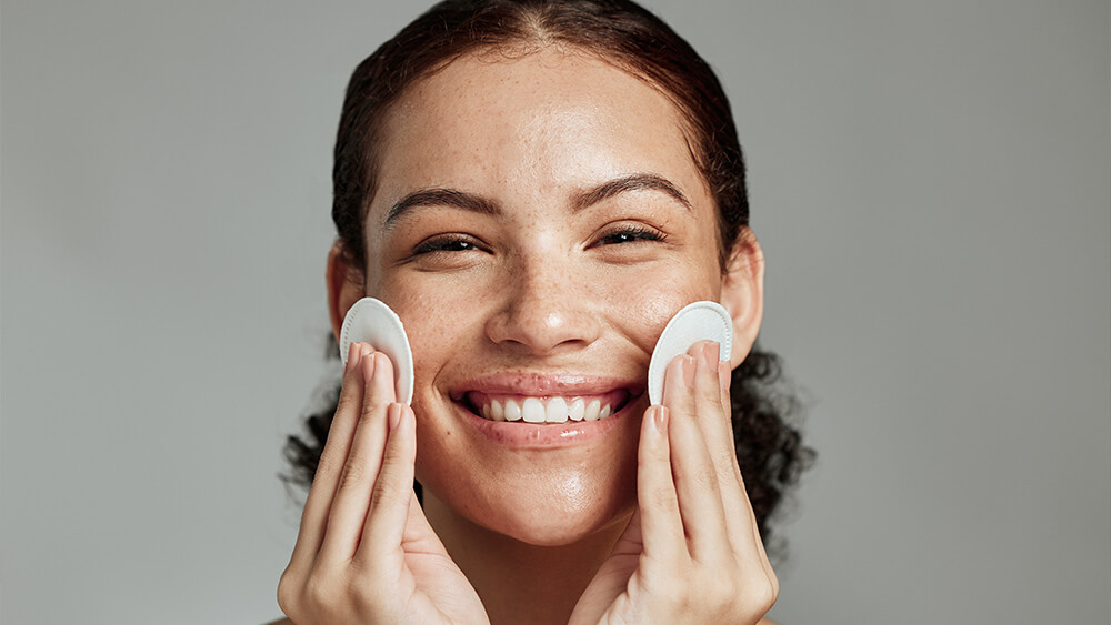 Happy woman cleaning her face with cotton pads