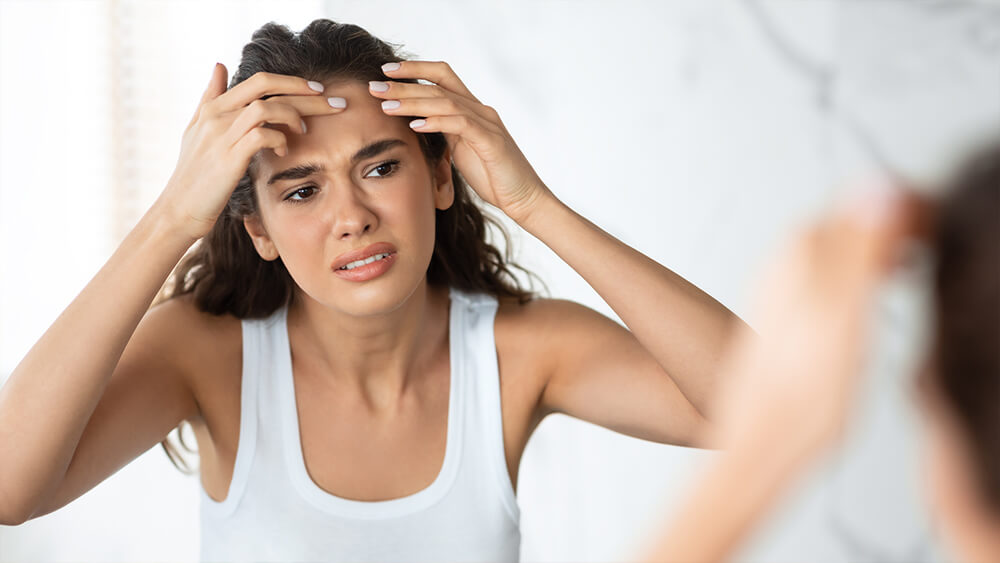 Sad woman with acne issue squeezing pimple