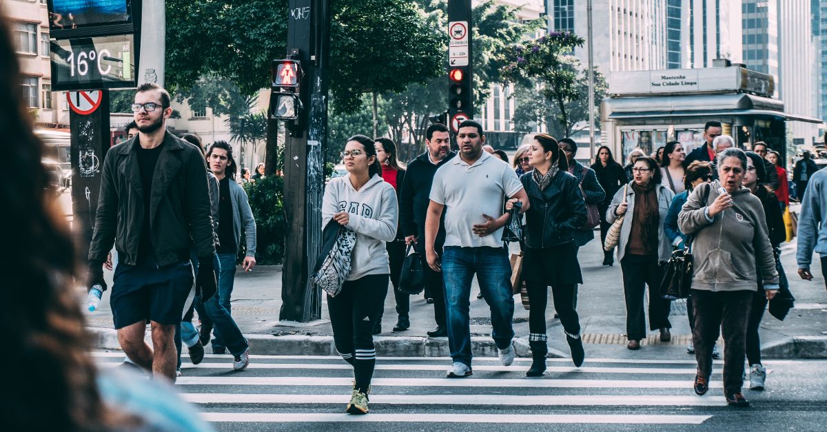 A pedestrian crosses a marked crosswalk while a car waits at the stop line